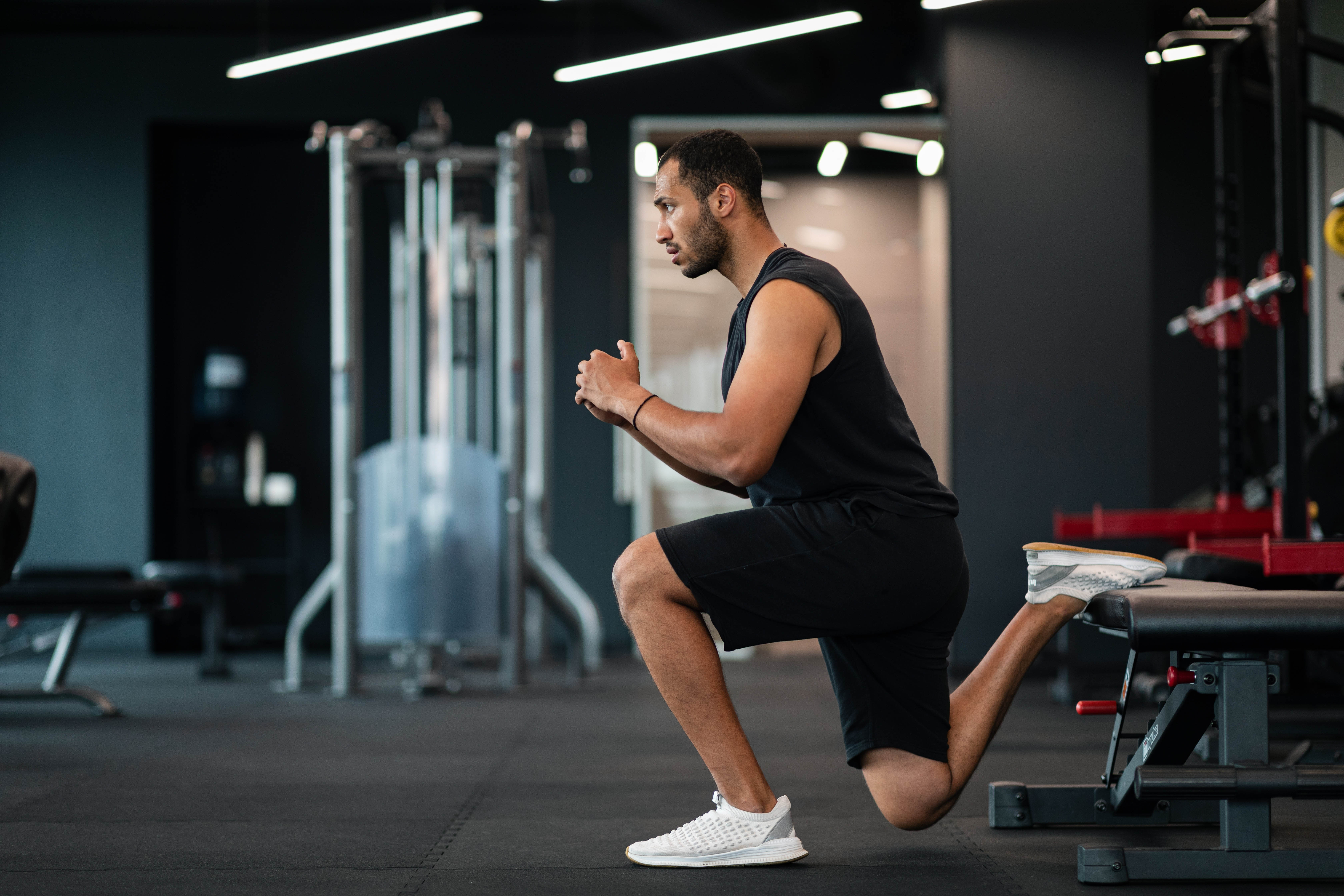 Man doing a split squat with a bench holding up one foot in the gym Man doing a split squat with a bench holding up one foot in the gym